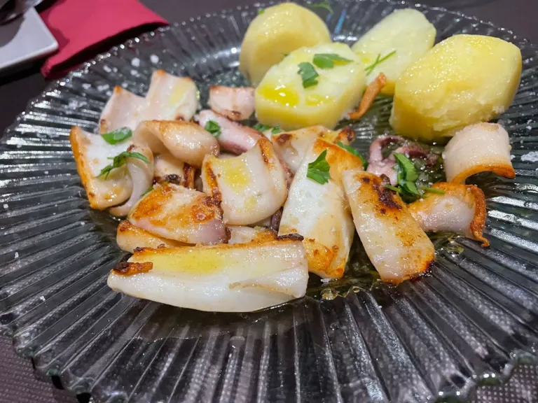 Un plato de calamares frescos a la plancha con unas patatas cocidas y espolvoreados de perejil.
