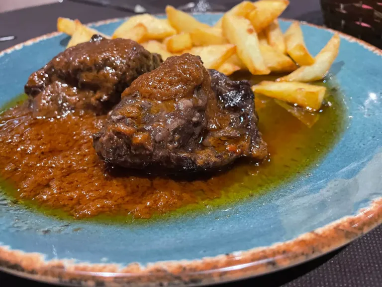 Un plato con carrilleras y patatas fritas.