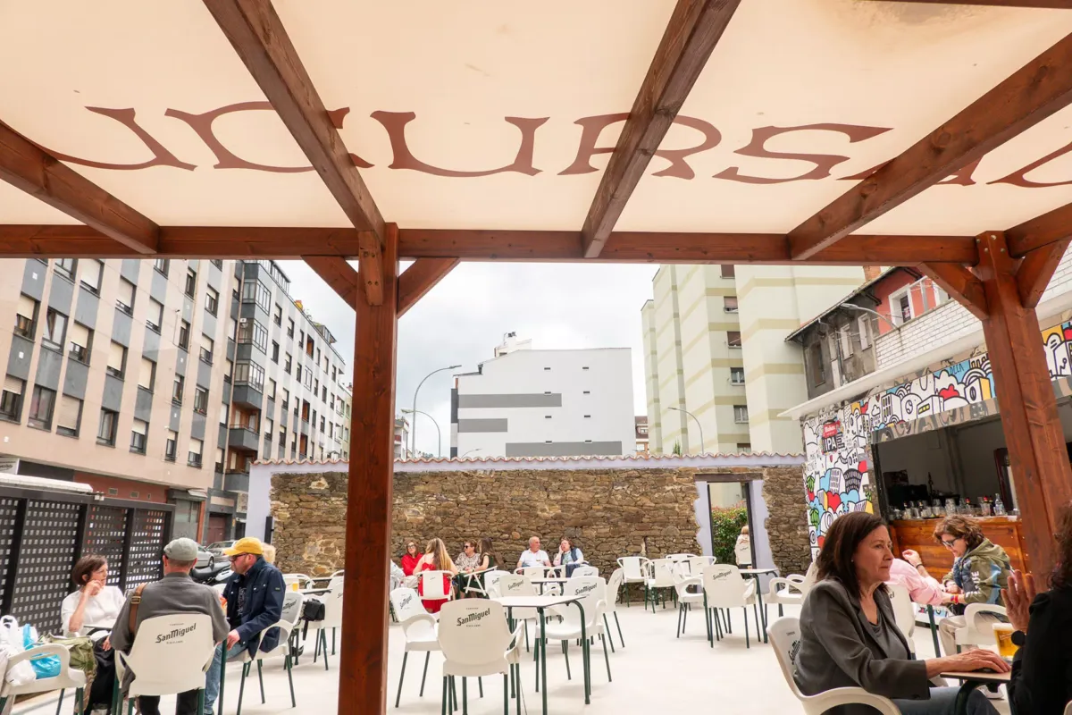 Terraza con toldo, a la derecha la barra y la gente en las mesas disfrutando de su bebida.