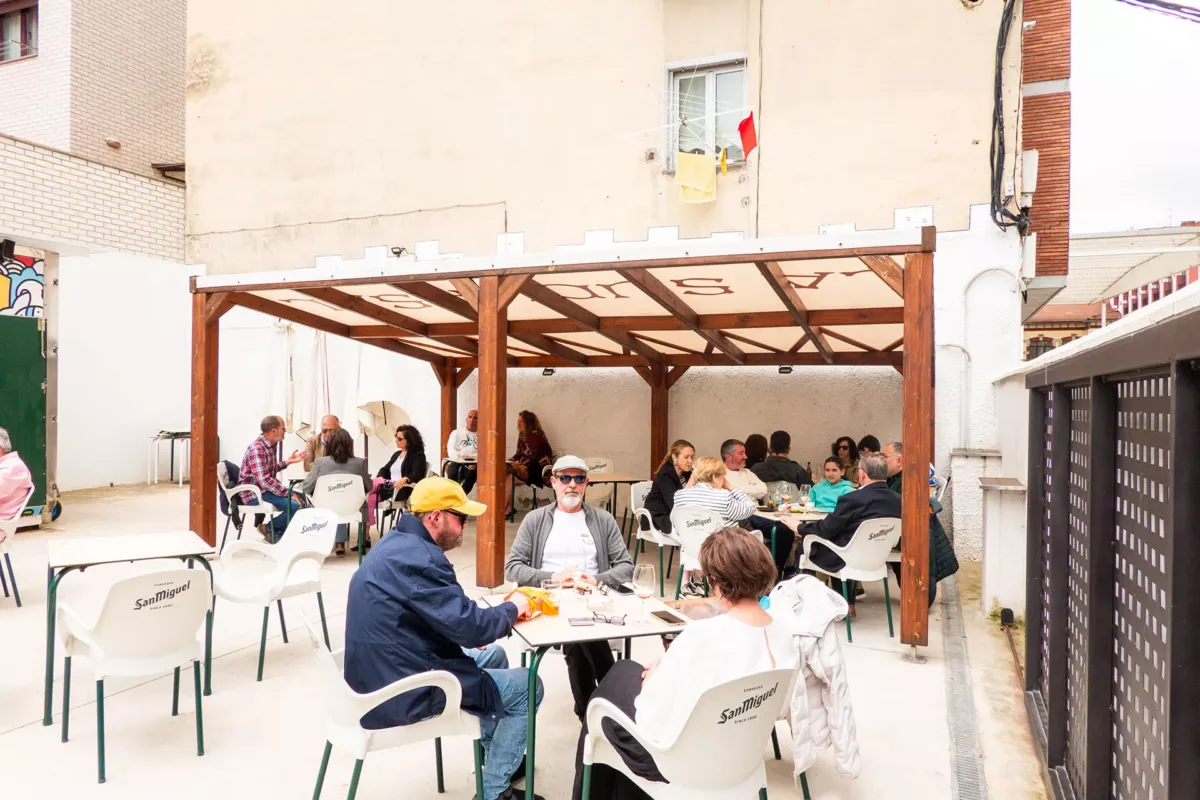 Terraza del Bar La Sucursal de Mieres con una parte cubierta por un toldo y gente sentada en mesas tomando el aperitivo.